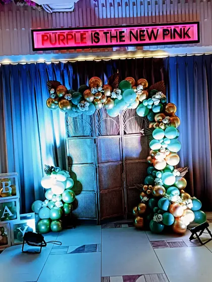 A bold and unconventional baby shower theme with the sign "Purple is the New Pink". The green and gold balloon arch against a rustic backdrop offers a stylish and edgy alternative to traditional colors.
