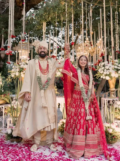 The couple celebrates their union with hands raised, standing on a carpet of pink petals under a beautiful floral mandap in Jaipur.
