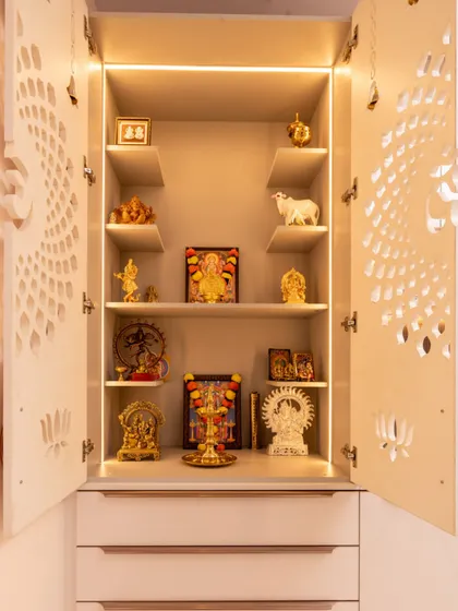 The inside of a beautifully organized pooja unit, with multiple shelves for idols and integrated lighting to create a divine glow.