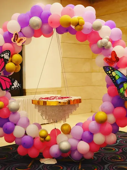 A close-up of a chandelier cake stand inside a butterfly-themed balloon ring. The colorful butterflies and balloons create a beautiful and unique focal point.