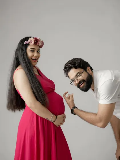A fun and interactive couple's pose, with the dad-to-be playfully pointing at the bump. The mom's bright dress and happy expression make this a joyful shot.