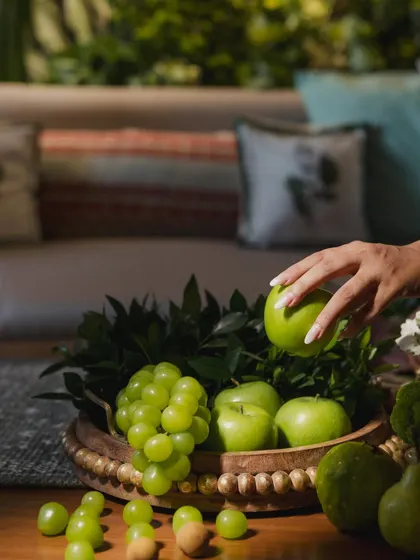 A detail shot from the Mehendi, with a hand reaching for a green apple from a bowl, highlighting the use of fresh, natural elements in the decor.