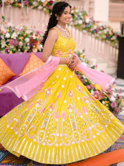 The bride twirls in her bright yellow and pink lehenga, her happiness radiating during a daytime Mehendi or Haldi event.