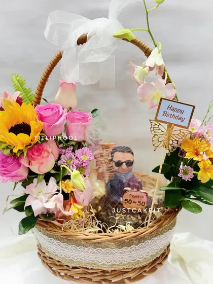 A 50th birthday hamper featuring a chocolate walnut cake with a half-figurine of the birthday person, nestled in a beautiful fresh flower basket.