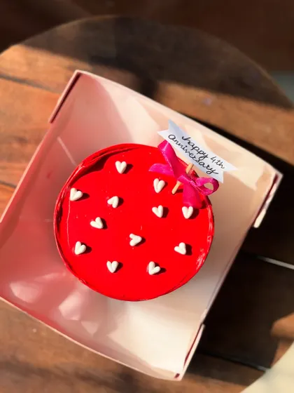 A vibrant red bento cake celebrating a 4th anniversary. Dotted with tiny white hearts and topped with a "Happy 4th Anniversary" flag, it’s a simple and sweet way to celebrate a milestone.