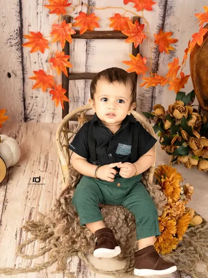 Our little autumn boy sitting in a wicker chair, surrounded by fall leaves and pumpkins.