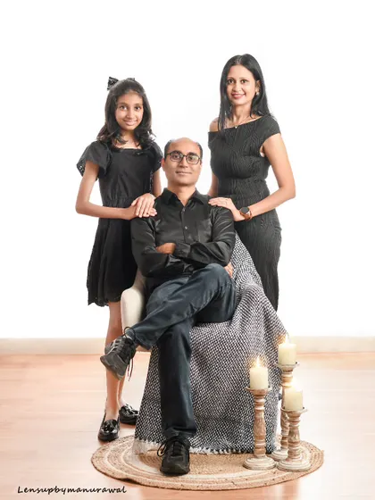 An elegant and classic family portrait. The father is seated while his wife and daughter stand beside him, all dressed in sophisticated black attire in a warmly lit studio.