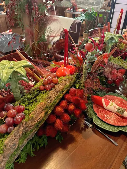A lavish, rustic tablescape for the Scarlett House launch party. A moss-covered log acts as a runner, overflowing with red flowers, grapes, and pomegranates.