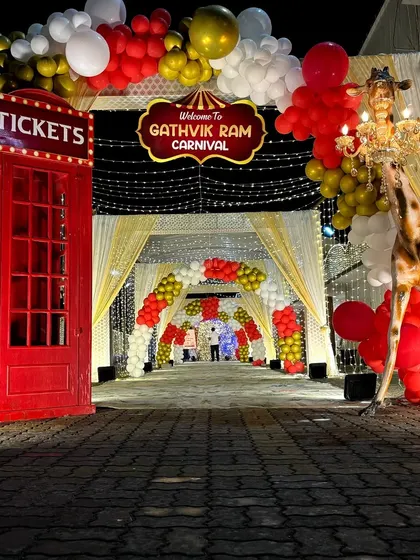 A dramatic nighttime entrance for a carnival party, featuring a red London telephone booth as a ticket stand and a life-size giraffe prop.