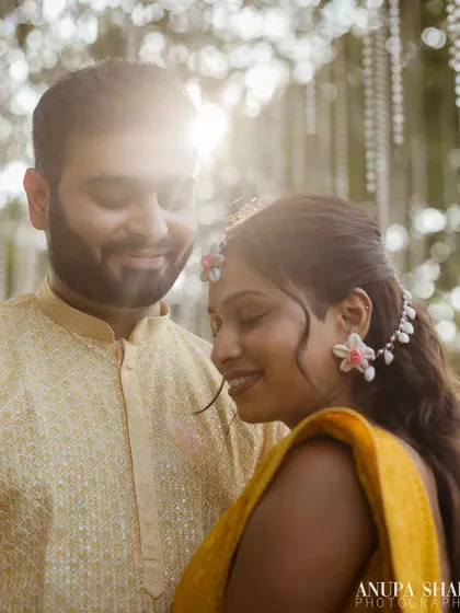 A soft, romantic close-up of the couple. The sun flares gently behind them, creating a dreamy, warm atmosphere for this Haldi portrait.
