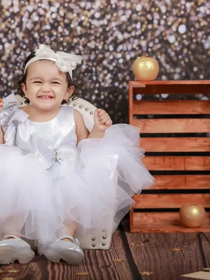 A little princess in a fluffy white dress beams with joy. The glittery background makes her shine even brighter in this happy, celebratory photo.