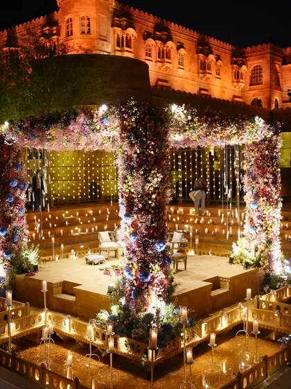 The wedding mandap at Suryagarh, Jaisalmer, illuminated by hundreds of candles against the palace backdrop. The structure is covered in a rich tapestry of flowers, creating a magical atmosphere for a nighttime ceremony.
