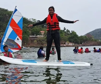 A young girl finds her balance on a stand-up paddleboard, surrounded by fellow campers and a windsurfer at our Karwar course.
