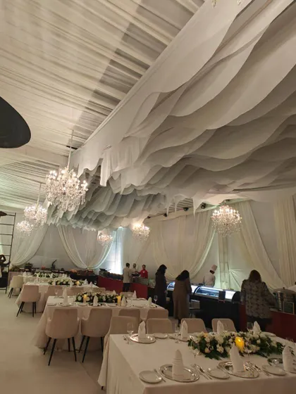 An all-white themed gala dinner featuring wavy ceiling drapes and multiple crystal chandeliers to create a dreamy, cloud-like effect. This setup is ideal for creating a clean, modern, and luxurious environment for corporate celebrations or award ceremonies.