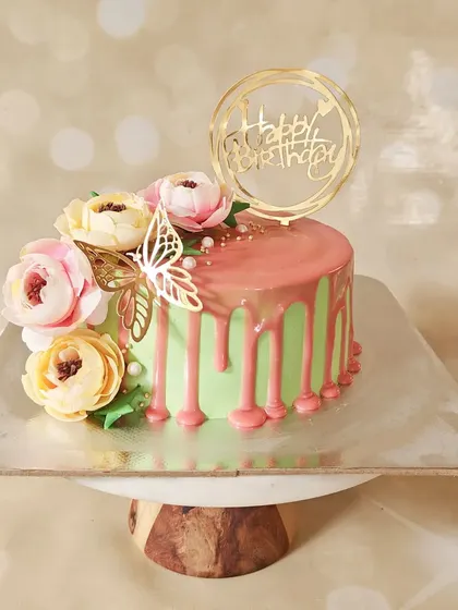 A lovely pastel green cake with a pink chocolate drip. The design is finished with a cascade of silk flowers and a golden butterfly, creating a soft and romantic feel.