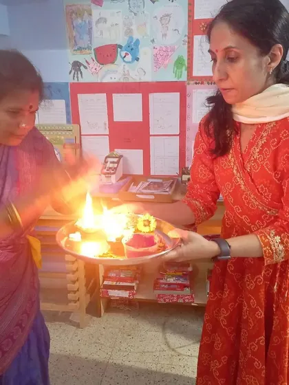 Two teachers perform the 'aarti' ceremony, holding a plate of lamps. This is a beautiful, sensory experience that brings the entire school community together.