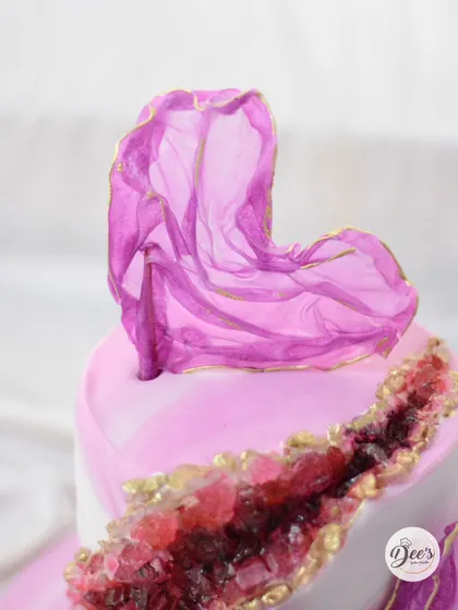 A close-up of the geode cake, showing the shimmering sugar crystals and the delicate, flowing rice paper sail with gold-painted edges.