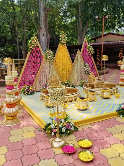 An elaborate Haldi setup with triangular backdrops, brass urlis, and traditional floral arrangements.