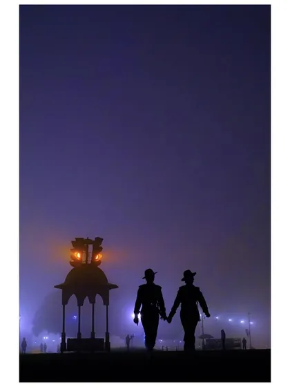 A silhouette of two soldiers holding hands as they walk through the fog during Republic Day rehearsals. The moody, purple twilight and the lantern create a poignant and atmospheric scene.