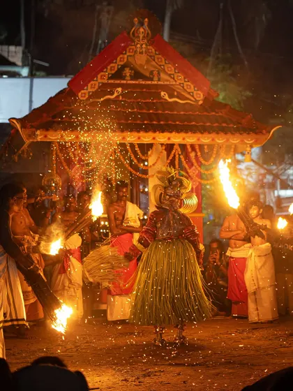 Images of the Pottan Theyyam dancing with torches in front of a small temple, or palliyara. The sparks flying around him create a mesmerizing spectacle of light and motion.