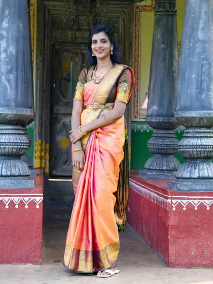 A beautiful portrait of the bride-to-be in a traditional silk saree, standing in a rustic, village-style doorway.