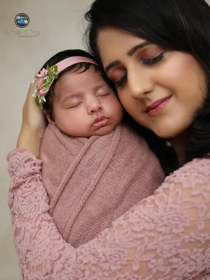 A peaceful moment captured between mother and her sleeping newborn. The soft lighting and coordinated pink outfits make this a truly heartwarming image.
