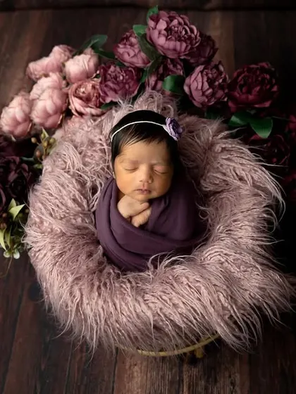 An overhead view of a newborn nestled in a purple-themed floral basket. The rich, dark colors create a moody and beautiful portrait.