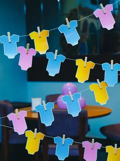 A close-up of a simple and cute decoration detail for a baby shower. These colorful baby onesie cutouts hanging on a line are an easy and effective way to add a playful touch to the decor.