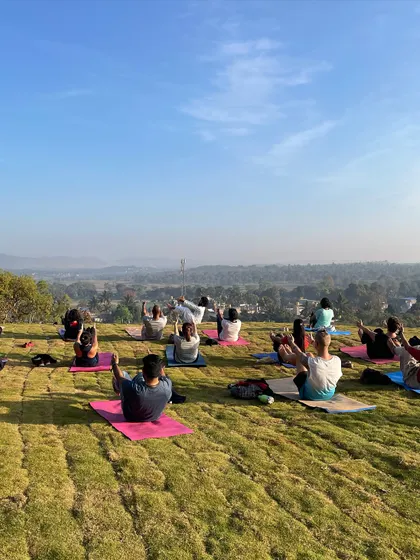 A group practicing Boat Pose (Navasana) on a grassy hilltop. This core-strengthening posture builds resilience and determination. The collective effort makes the challenge more enjoyable.
