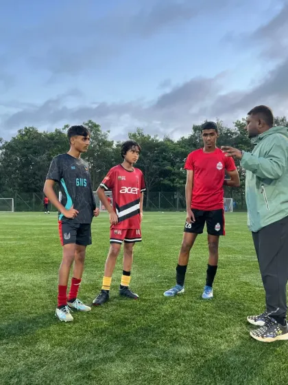 A coach giving one-on-one tactical advice to a small group of players on the training ground.