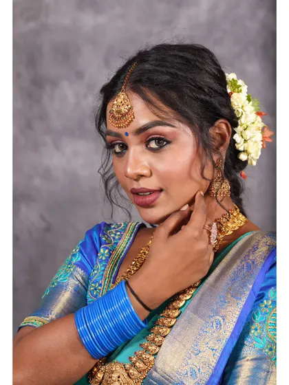 A beautiful studio portrait featuring a blue silk saree. The lighting highlights the texture of the fabric and the traditional jewelry.