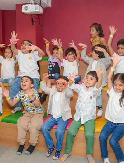 A group of kids enthusiastically participates in a guided activity, with their hands in the air.