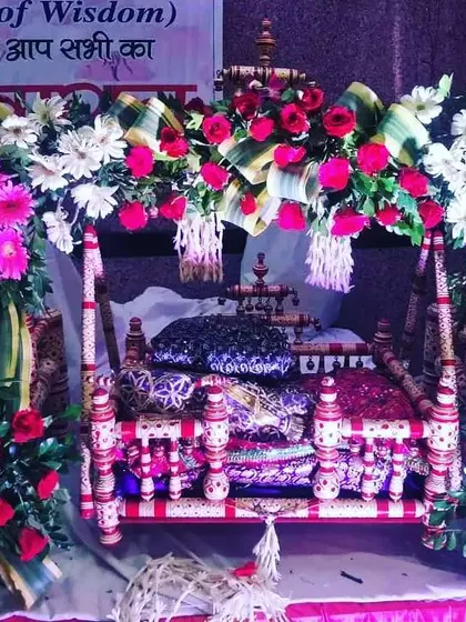 A close-up of a decorated jhula for Ladoo Gopal. The cradle is adorned with bright pink roses and white gerberas, ready for the Janmashtami festivities.
