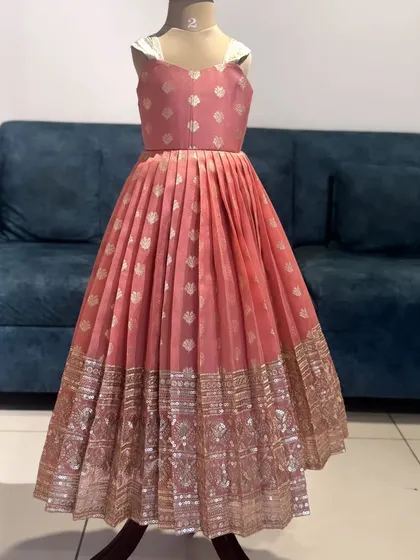 Here's the dress on its own, showcasing the craftsmanship. This peach brocade frock features a beautiful pleated skirt and a detailed gold border, designed to be both lightweight and stunning.