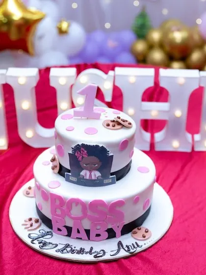A 'Boss Baby' themed two-tier cake set in front of light-up letters spelling the birthday girl's name. We compose our shots to show how different decor elements work together.