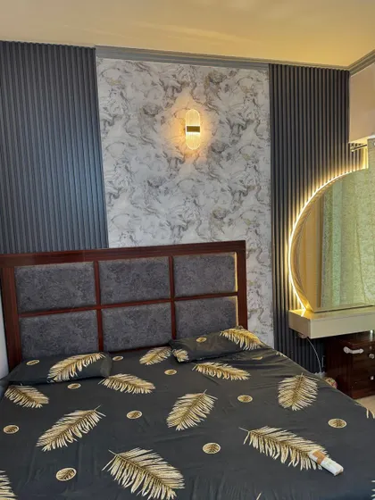 A bedroom design with a feature wall combining grey fluted panels and a marble-finish wallpaper. The round backlit mirror serves as a stylish dressing area.
