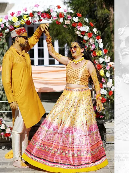 A joyful shot of the couple dancing under a floral arch at their Haldi ceremony. Their happiness is contagious.