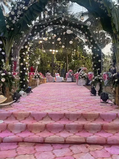 A beautiful pink-themed aisle leading up to a mandap decorated with banana leaves and florals. The lotus-shaped floor lamps add a unique and elegant touch to the pathway.