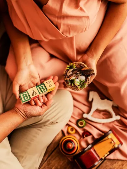 A detailed flat-lay style shot focusing on the hands of the couple holding baby blocks and a tiny nest. This artistic composition is rich with symbolism about building a home and nurturing new life.
