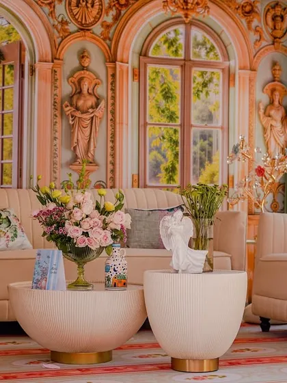 A romantic seating area framed by ornate white pillars. The backdrop is a painted mural of a European garden, creating a beautiful and immersive photo opportunity.