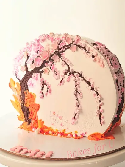 A stunning cake featuring a hand-painted cherry blossom tree. The delicate pink blossoms are piped with buttercream, creating a beautiful and artistic centerpiece.