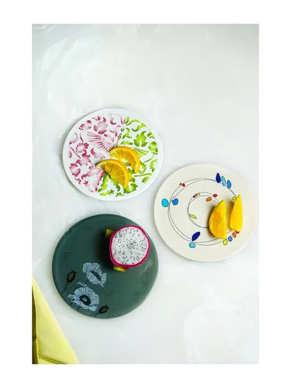 A top-down view of three different artisanal plates, each styled with fresh fruit. This is an effective way to showcase multiple designs from a collection in one shot.
