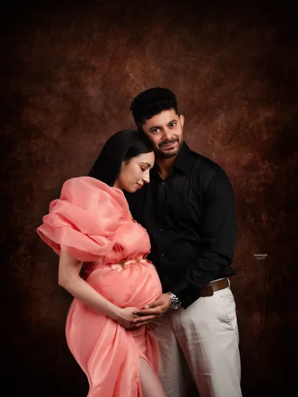 An intimate and tender moment between partners. The close embrace and soft lighting against the dark backdrop create a deeply emotional and romantic maternity portrait.