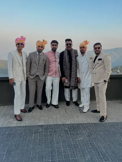 The groom's squad at a destination wedding, all dressed in our custom designs. The group showcases a mix of styles, including double-breasted suits, classic sherwanis, and a Jodhpuri jacket, all coordinated in a neutral color palette.