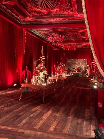 A wide shot of the hall decorated in the royal red theme. You can see how the consistent use of red drapery, wooden flooring, and intricate ceiling details creates a cohesive and grand atmosphere for a luxury wedding.