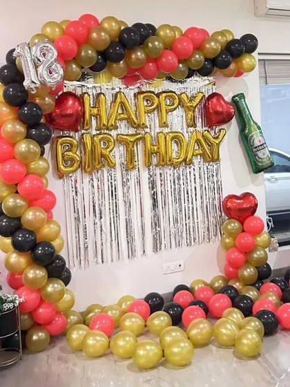 An 18th birthday party setup with a red, black, and gold balloon frame around a silver shimmer curtain.