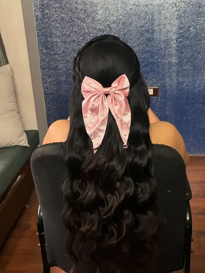 A half-up hairstyle with a small braid and a large pink bow, perfect for a fun and youthful look.