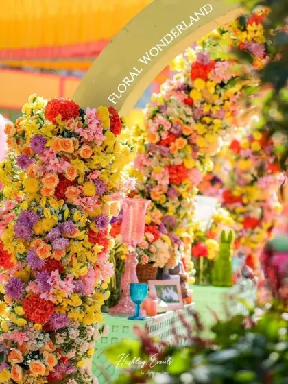 A close-up of a floral archway from a "Floral Wonderland" themed event. The arch is densely packed with a rainbow of flowers, creating a stunning and immersive experience.