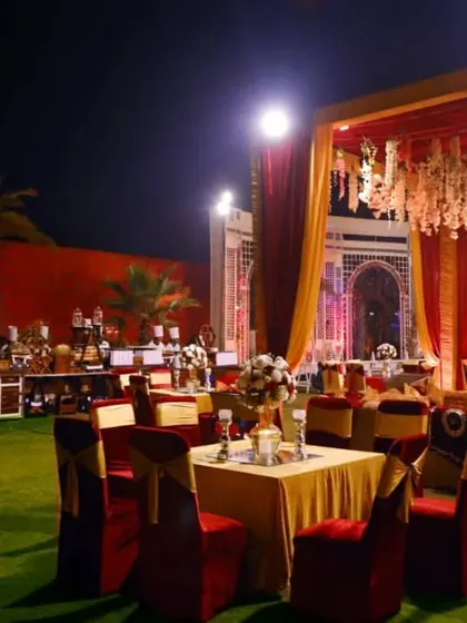 An outdoor reception setup with luxurious red and gold seating, set against an illuminated palace-like facade.