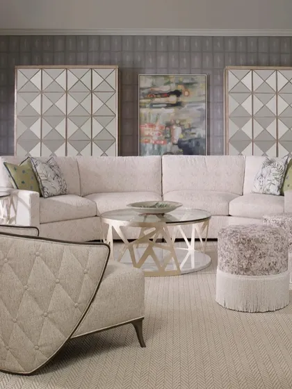 A full living room setting, showcasing our graceful winged lounge chair, a large sectional sofa, and fringed ottomans. The buttoned and tufted detailing on the chair's exterior adds a layer of classic craftsmanship.